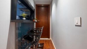 Un couloir étroit, avec une porte en bois au fond, une petite table entourée de chaises et une plante en pot posée sur une étagère.