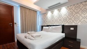 Une chambre d’hôtel avec un grand lit, une table de chevet sombre, une porte en bois et un mur à motifs.