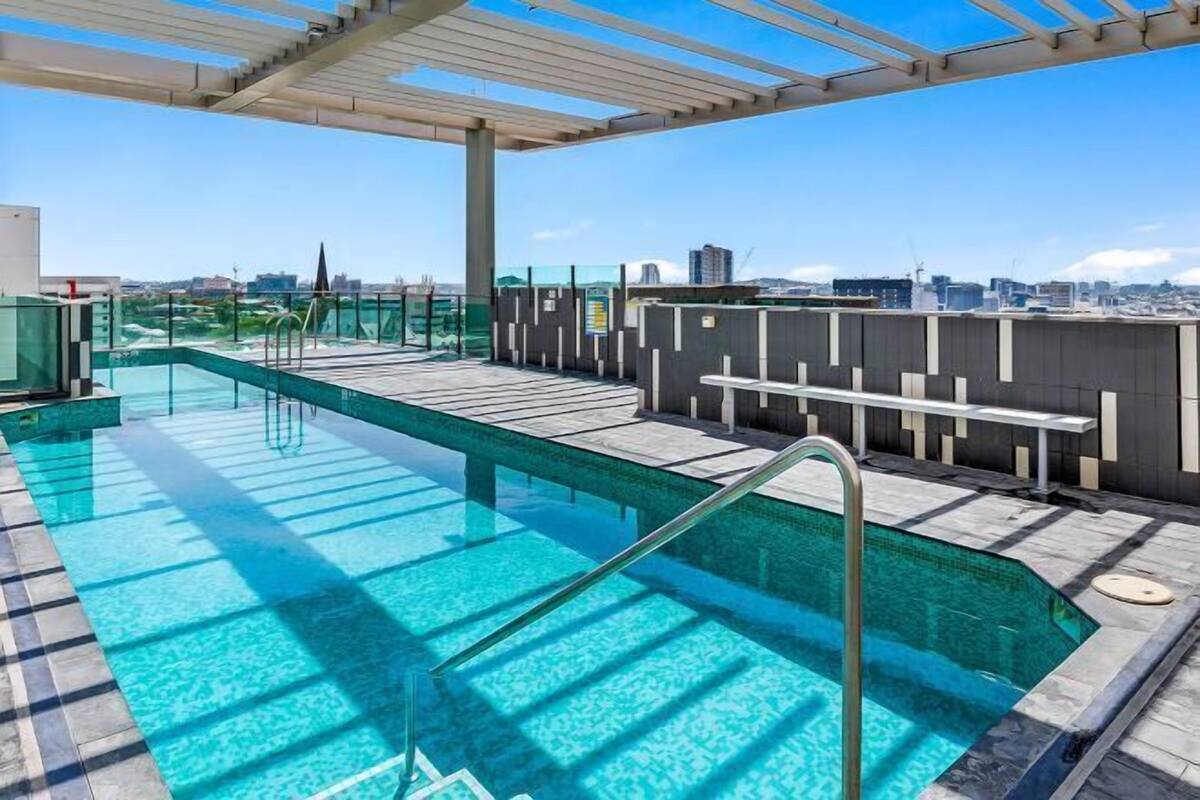 Ein Dachpool mit klarem, blauem Wasser, einer Pergola darüber und einer Blick auf die Stadt im Hintergrund.