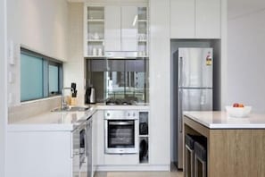 A modern kitchen with white cabinetry, stainless steel appliances, and a built-in oven.
