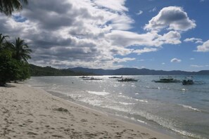 Una playa con cielos despejados, aguas tranquilas y barcos.