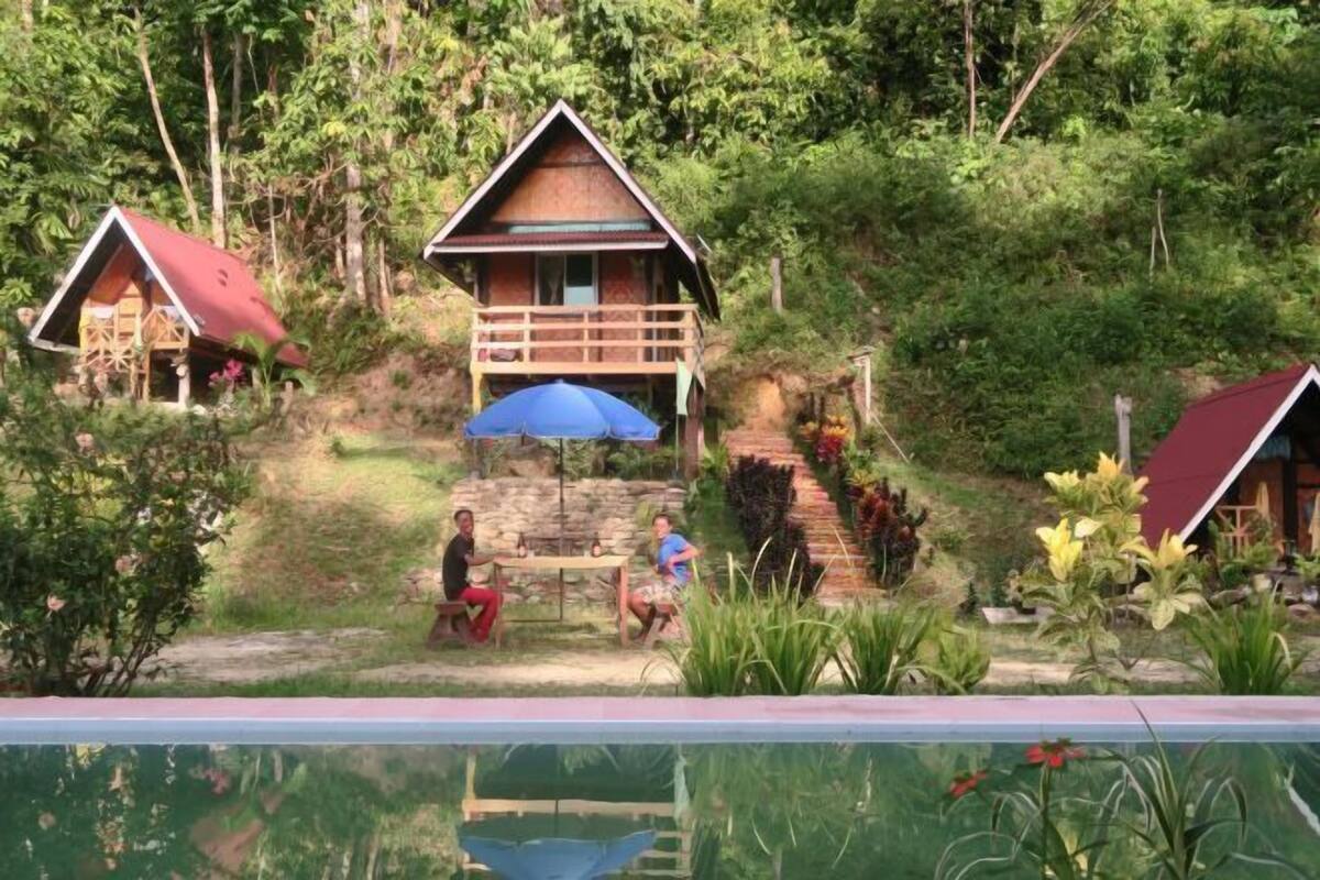 Ein Bungalow mit Balkon, umgeben von üppiger Vegetation und einem Schwimmbecken.