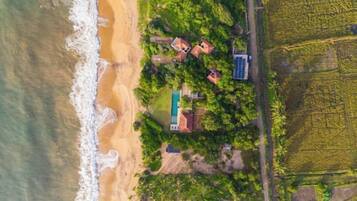 An aerial view of a coastal property with a beach, a swimming pool, and surrounding vegetation.