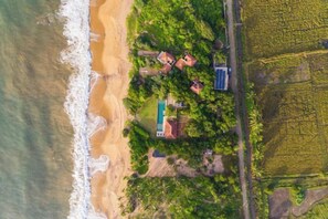 An aerial view of a coastal property with a beach, a swimming pool, and surrounding vegetation. - Ravana Garden (Hambantota)