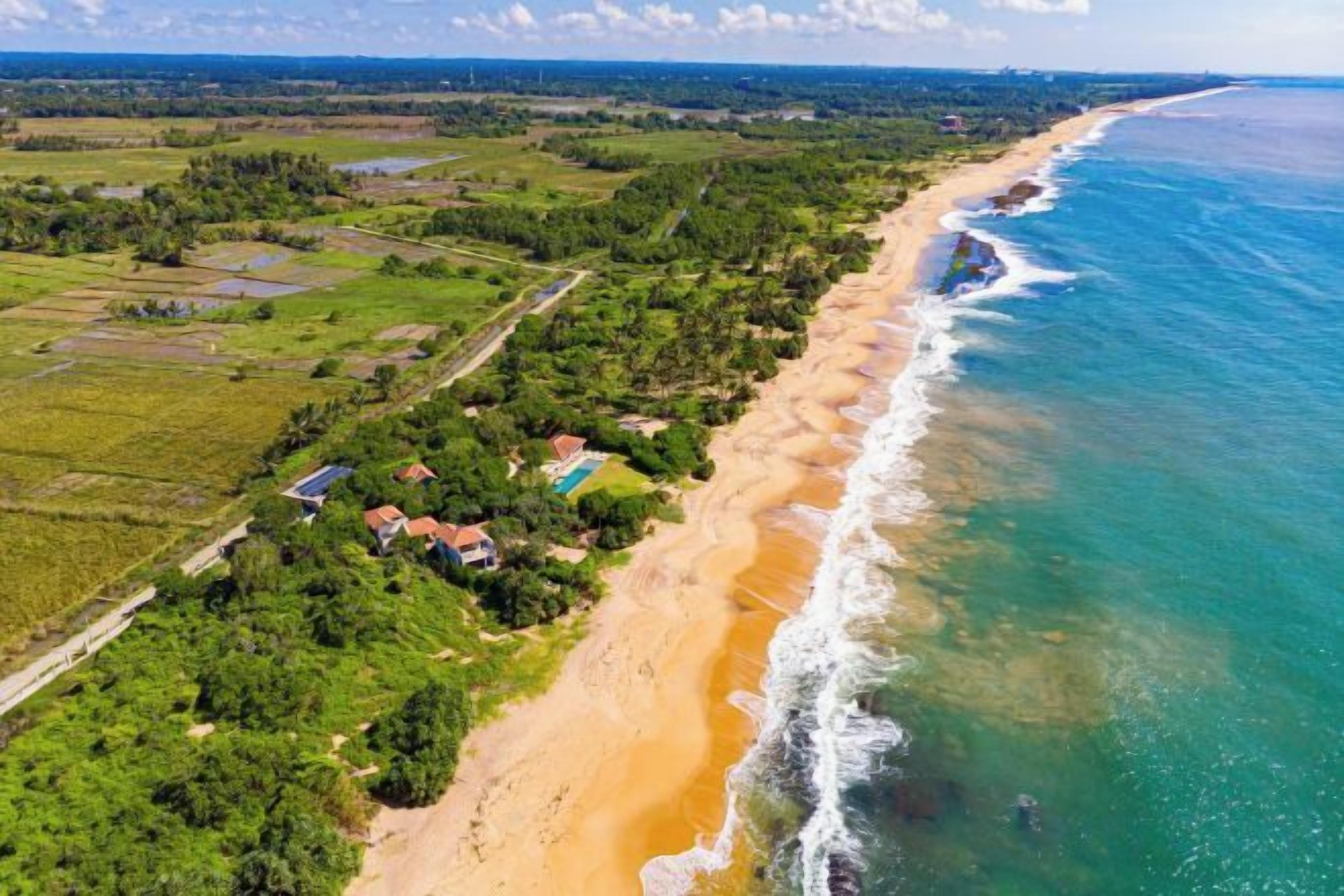 An aerial view of a coastal area with a beach, houses, and greenery.