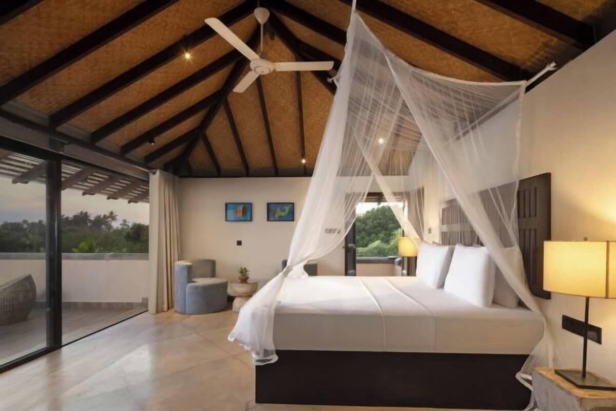A bedroom with a bed, a ceiling fan, a nightstand, and a view of the outdoors.
