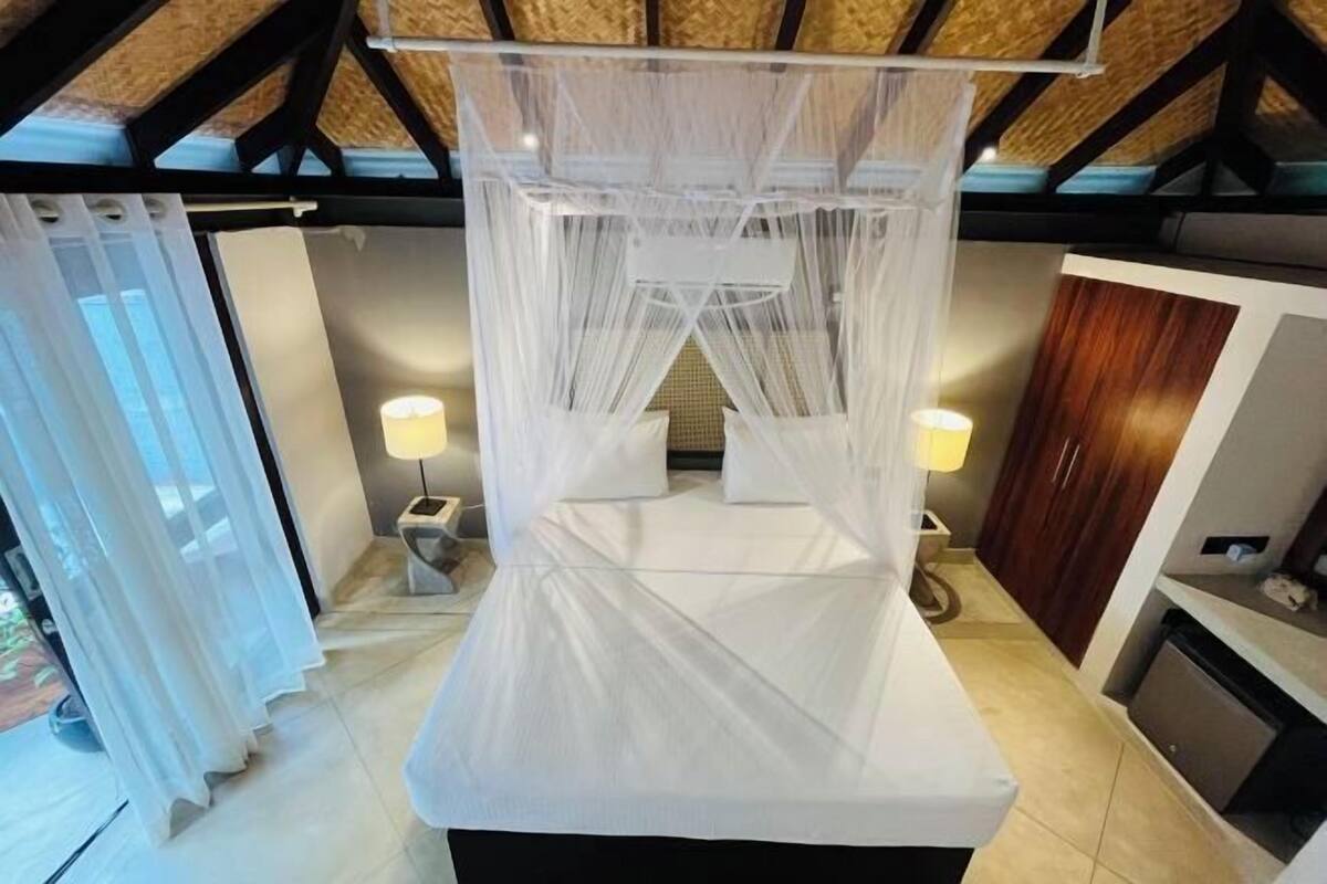 A bedroom with a canopy bed, two bedside lamps, a small bedside table, and a wooden wardrobe.