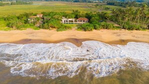 A coastal property with a beach view, a house surrounded by greenery, and waves approaching the shore. - Ravana Garden (Hambantota)