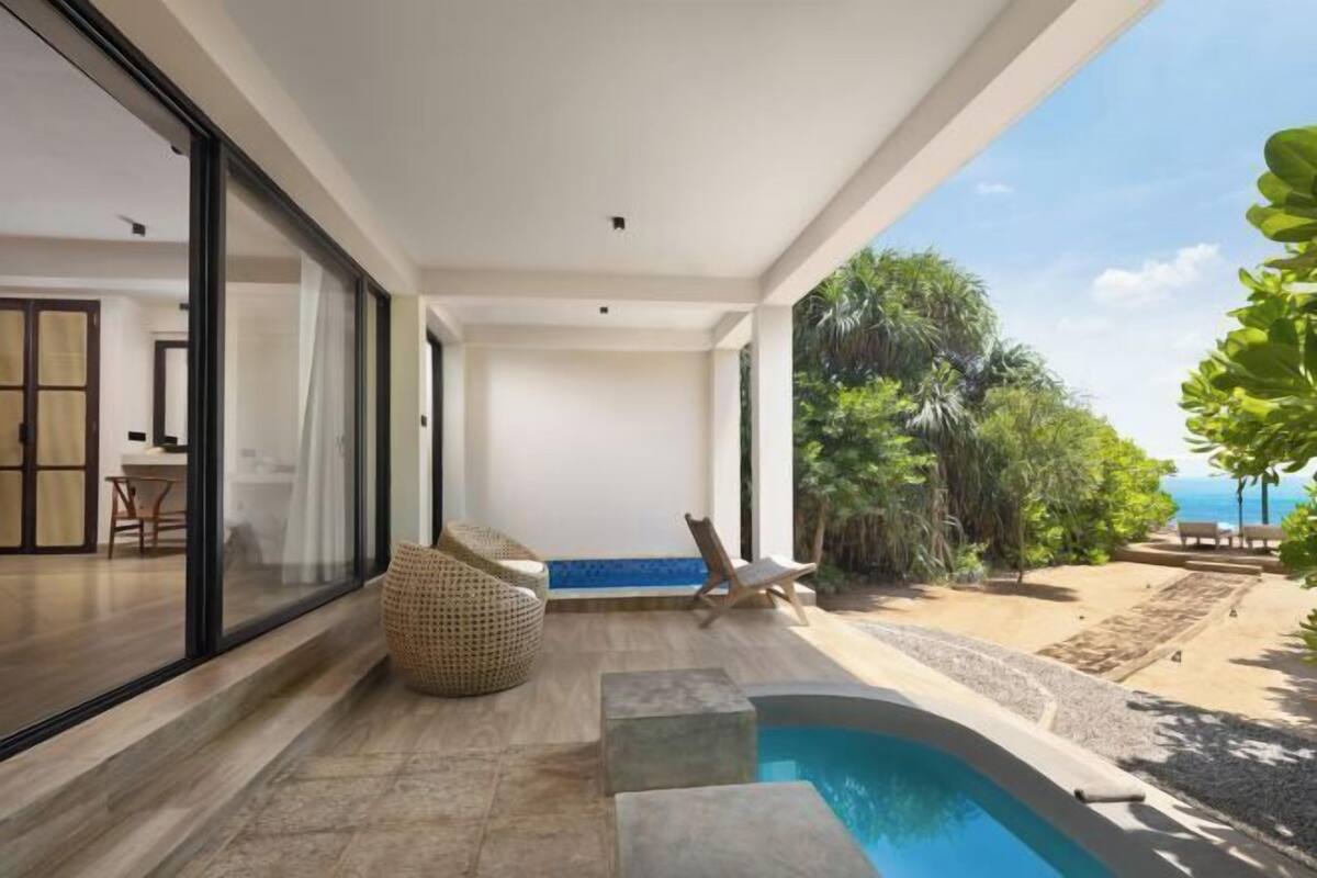 A modern outdoor pool area with a clear view of the sea, a lounge chair, and a wicker seating area.