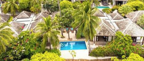 A resort with multiple bungalow-style accommodations, a central swimming pool, and lush tropical landscaping.