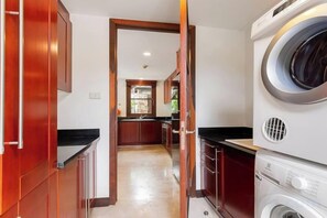Un área de lavandería con lavadoras apiladas y una puerta de madera que da a una cocina.
