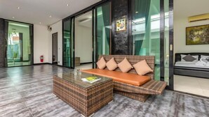 A modern interior with a glass partition, a wicker sofa with cushions, a glass coffee table, and a bed with a headboard.
