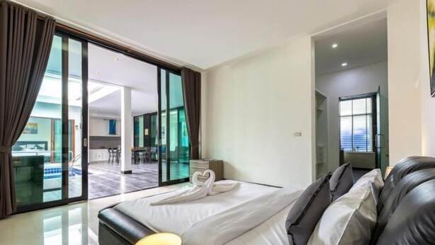 A modern hotel room with a large bed, a glass door leading to a balcony, and a visible dining area.
