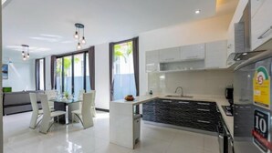 A modern kitchen with white cabinets, a central island, and a dining area with white chairs.