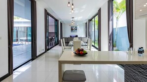 A modern dining area with a long table, chairs, and a fruit bowl.