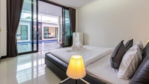 A hotel room with a bed, a bedside lamp, a view of a pool through a glass door, and a white towel on the bed.