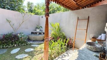 A covered outdoor area with a concrete wall, a wooden ladder, a stone basin, and various plants.