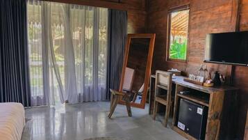 A room with a bed, a television, a desk with a computer, and a window with curtains.