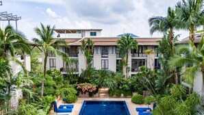 A pool area with blue lounge chairs and a rectangular pool, surrounded by lush greenery and palm trees. - Phuket Royal Marina & Resort 4 bedroom Penthouse (Phuket)