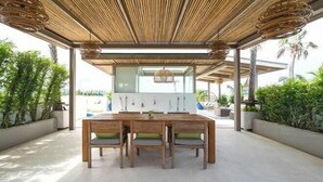 An outdoor dining area with a wooden table and chairs, surrounded by potted plants and a bamboo ceiling. - Phuket Royal Marina & Resort 4 bedroom Penthouse (Phuket)