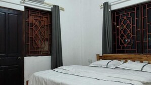 Ein Zimmer mit einem Bett, einem hölzernen Kopfende, einem Fenster mit dekorativem Gitter und einer Tür mit ähnlichem Gitter.
