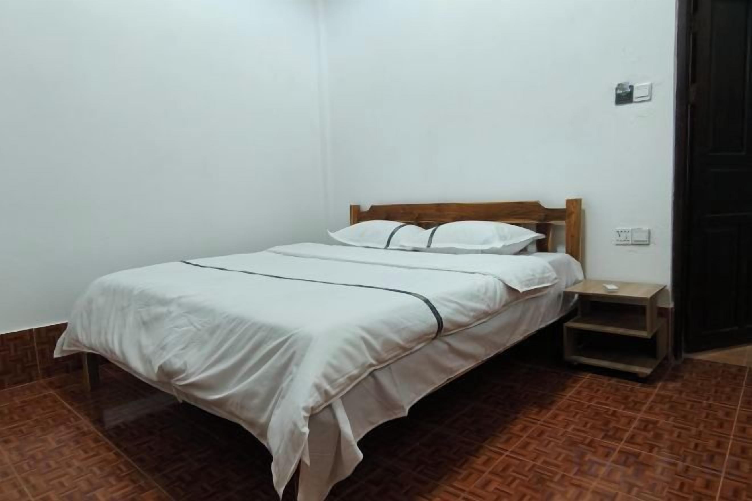 A single bed with a wooden headboard in a room with white walls and brown flooring.