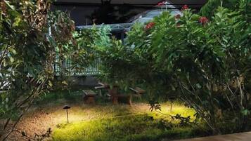 An outdoor garden area with a wooden bench, a small table, and a lamp post.