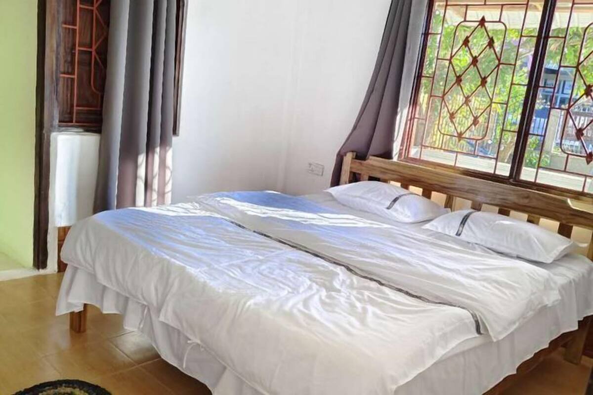 A bed with white bedding, a wooden headboard, and a window with a view of greenery.