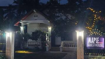 A house with a porch, a sign reading "Maple Guesthouse," and a well-lit entrance.