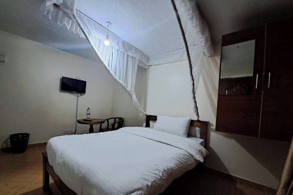 Un dormitorio con cama, televisor, mesita y armario.