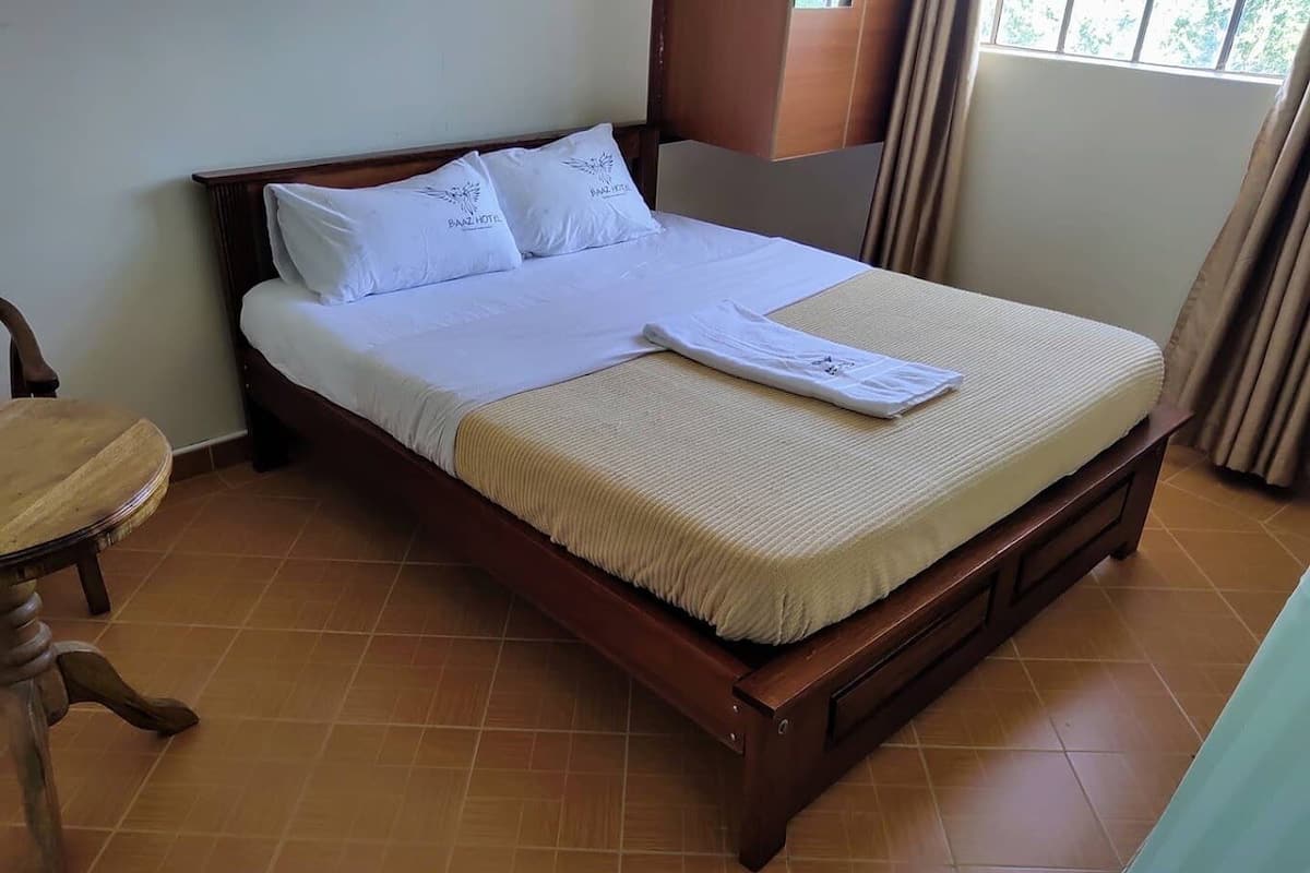 Una cama bien tendida con ropa blanca y almohadas, un cabecero de madera y una silla de madera a su lado.