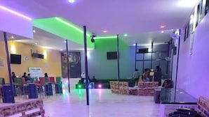 A spacious indoor area with wooden benches and tables, a green-lit ceiling, and a seating area with chairs and tables. - Baaz Hotel Kakamega (Kakamega)