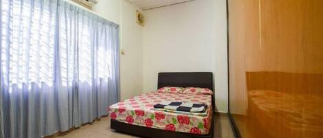 A bedroom with a bed, curtains, an air conditioning unit, and a wooden wardrobe.