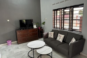 Una sala de estar con un sofá, dos mesas redondas, un televisor sobre un mueble de madera y una ventana con rejas.