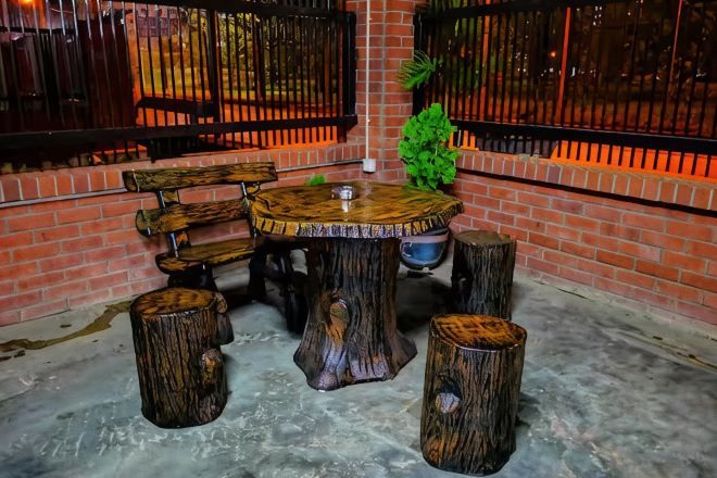 Un'area salotto esterna rustica con un tavolo di legno rotondo e panche, circondata da sgabelli fatti con tronchi d'albero.
