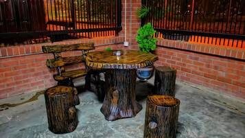 Un'area salotto esterna rustica con un tavolo di legno rotondo e panche, circondata da sgabelli fatti con tronchi d'albero.