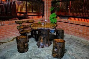 Ein rustikaler Außenbereich mit Sitzgelegenheit, bestehend aus einem runden Holztisch und Bänken, umgeben von Hockstühlen aus Baumstämmen.