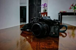 A camera on a wooden floor with a door and a small table with flowers in the background. - 63 Guesthouse (Jalan Bakri)