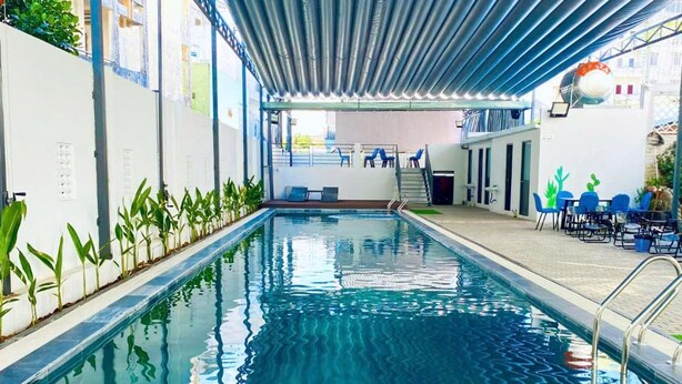 An indoor swimming pool with a covered area, a seating area with chairs, and a staircase leading to an upper level. - Apple Hotel (Can Tho)