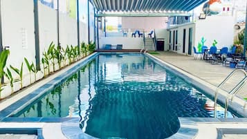 Une piscine intérieure dotée d’une zone couverte, d’un espace détente avec des chaises et d’un escalier menant à un niveau supérieur.