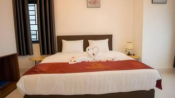 A hotel room with a large bed, a nightstand, a lamp, and a window with curtains.