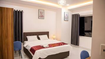 A modern hotel room with a large bed, a bedside table, a lamp, and a window with curtains.