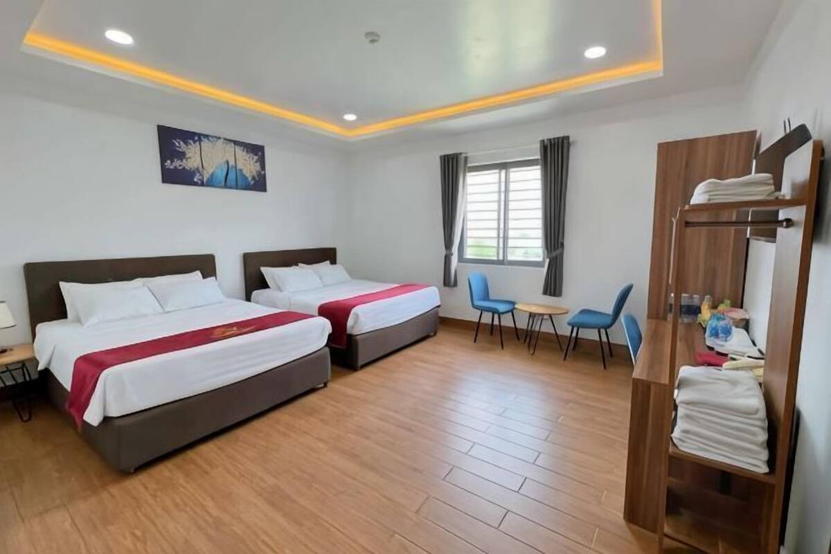 A hotel room with two beds, a desk, a chair, a wardrobe, and a window with curtains.