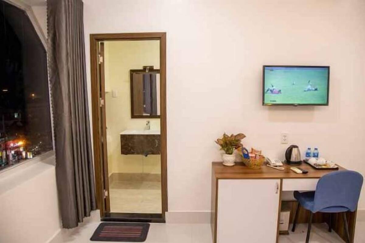 A hotel room with a desk, chair, television, and a view of the city at night.