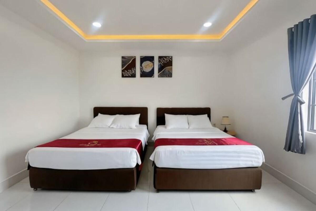 A hotel room with two beds, a ceiling light, and a window with curtains.