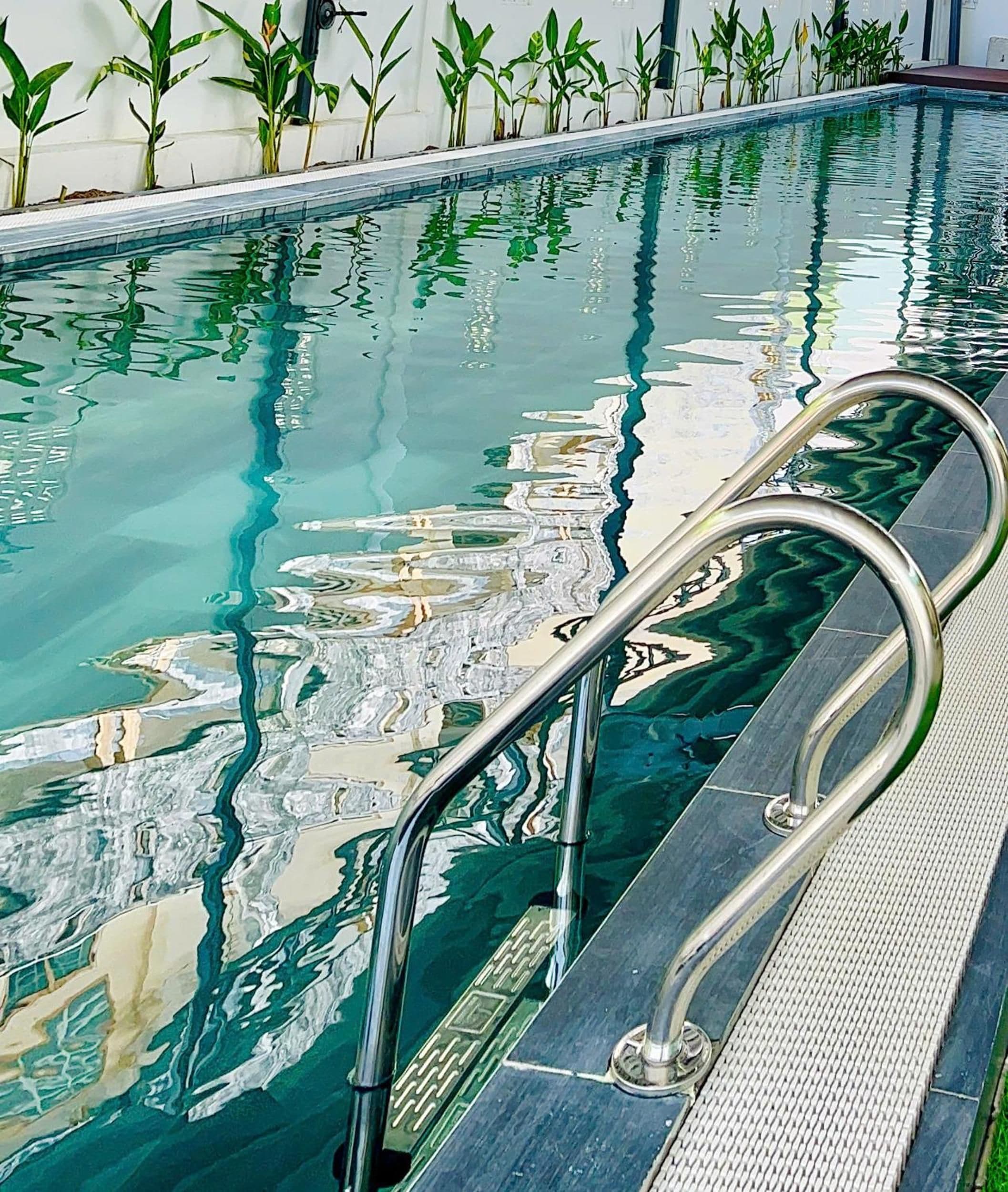 A swimming pool with clear water, metal handrails, and a tiled deck.
