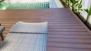 A pool area with a wooden deck, lounge chairs, and potted plants.