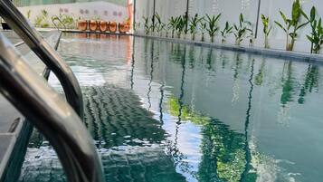 A swimming pool with clear water, surrounded by a white wall with small windows and plants.
