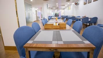 A conference room with a long table, blue chairs, and a Christmas tree in the background.