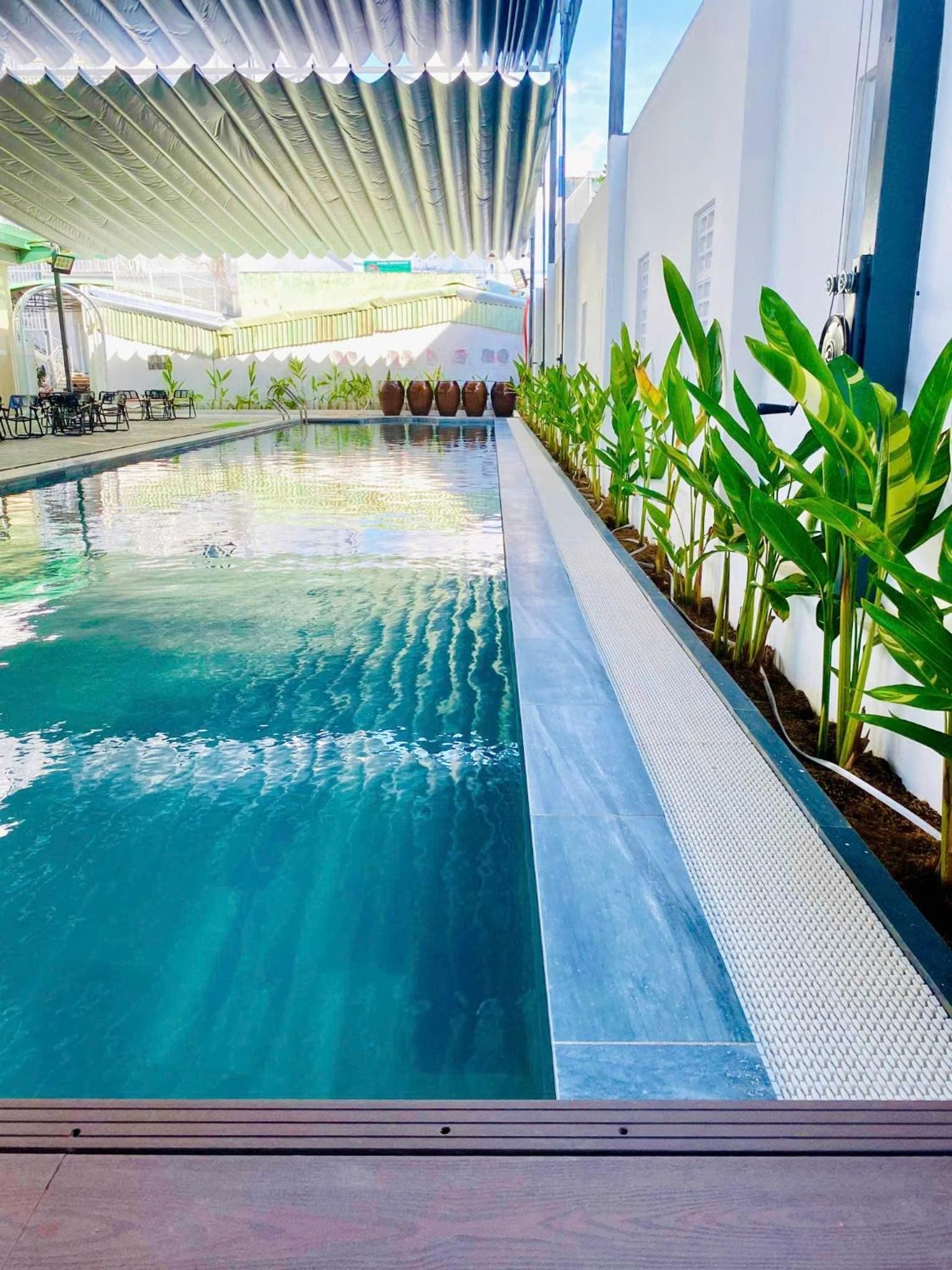 A swimming pool with a tiled edge, surrounded by potted plants and a covered area with a white ceiling.